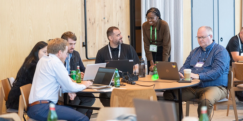 People siting on a table using laptops at Benchmark Gensuite's conference